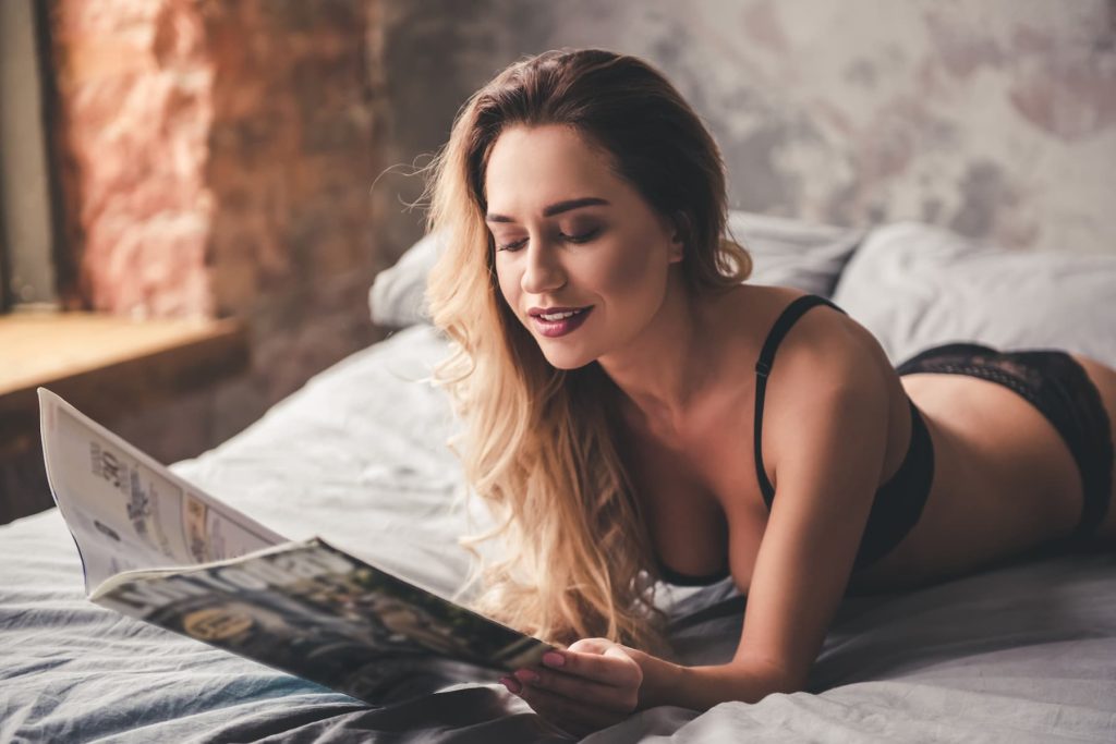 Femme sexy en lingerie allongée dans son lit lisant un magazine.